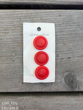 Load image into Gallery viewer, A set of three red plastic buttons on their original button card against a wood background.