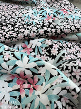 Load image into Gallery viewer, Pastel pink and blue colored flowers are printed on fabric with a crepe texture and a black background.
