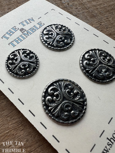 Four ornate scandinavian silver buttons on a card labeled 'The Tin Thimble' on a wooden surface.