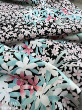 Load image into Gallery viewer, Pastel pink and blue colored flowers are printed on fabric with a crepe texture and a black background.
