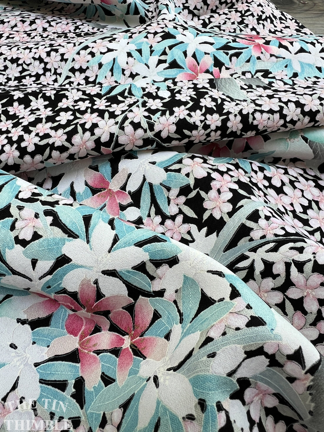 Pastel pink and blue colored flowers are printed on fabric with a crepe texture and a black background.